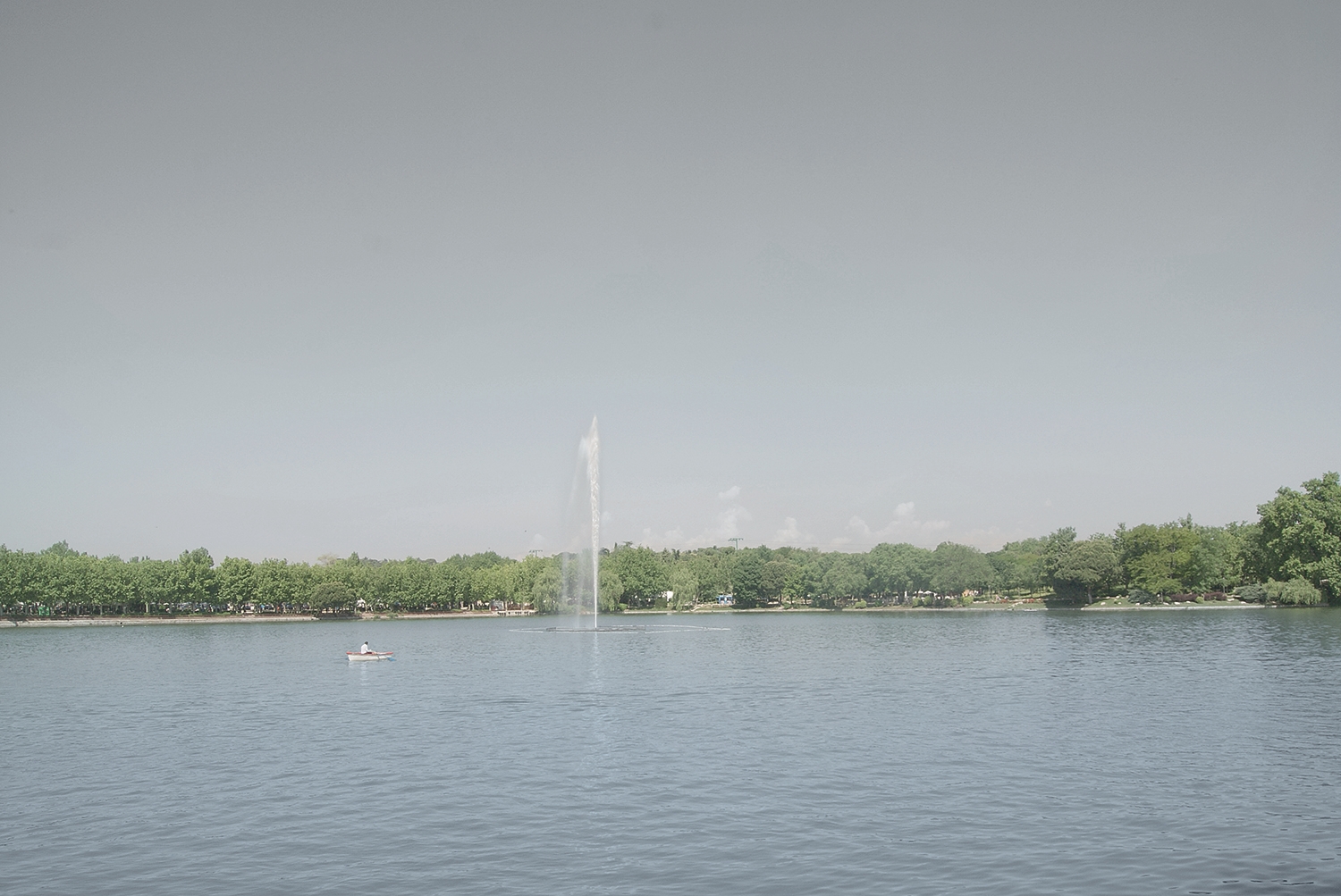 Wide view of lake with fountain in urban park landscape, A Man in a Park.