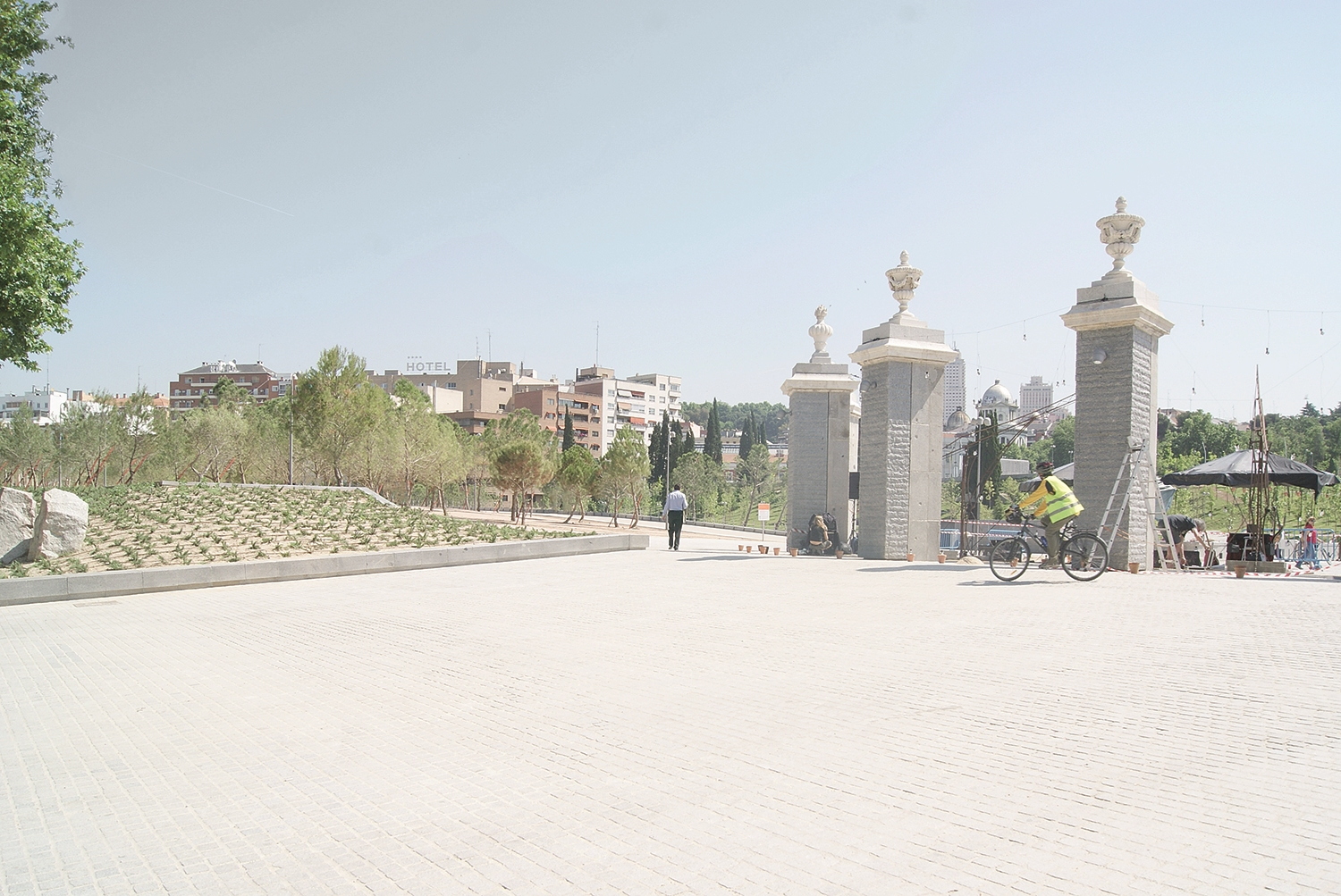 A Man in A Part. Park entrance gate with cyclists and open urban space.