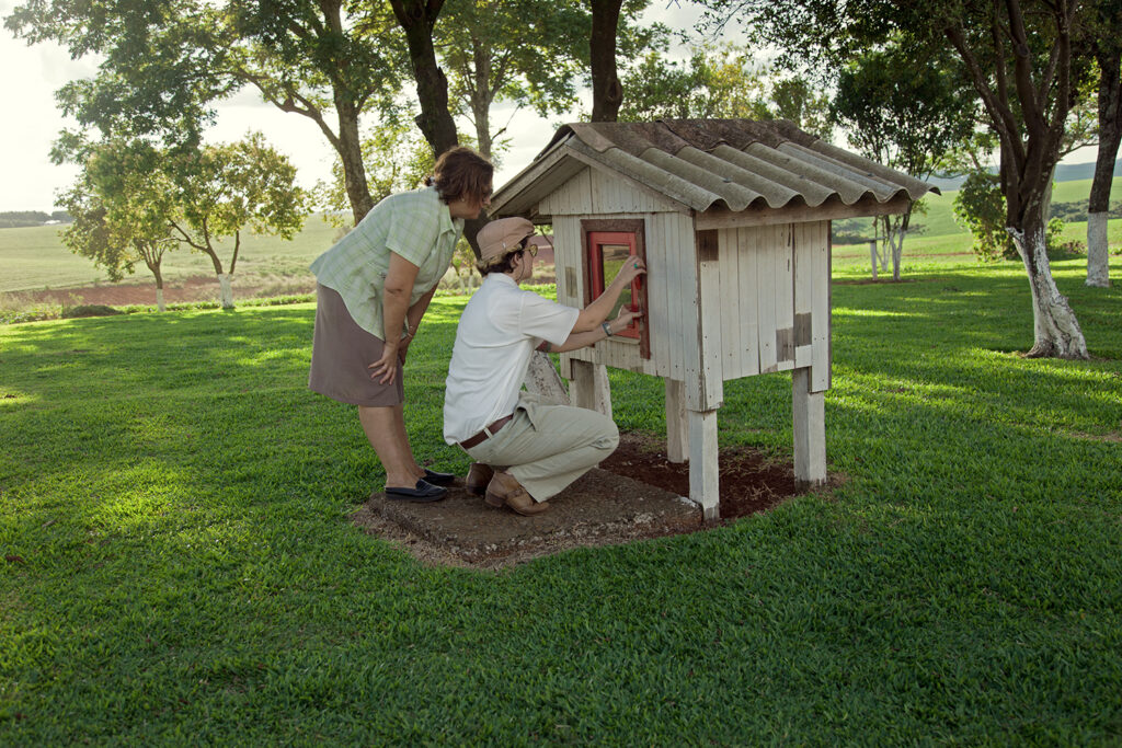 Two people adjusting a small wooden structure in a green yard, O Destino de Um Coração