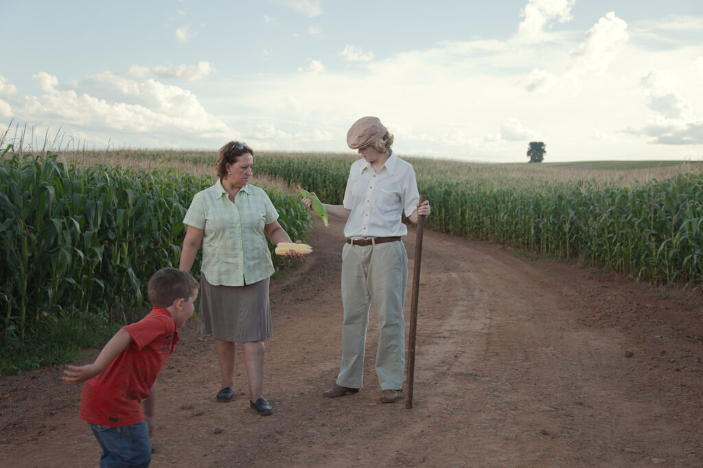Three generations standing on a rural road beside a cornfield, O Destino de Um Coração